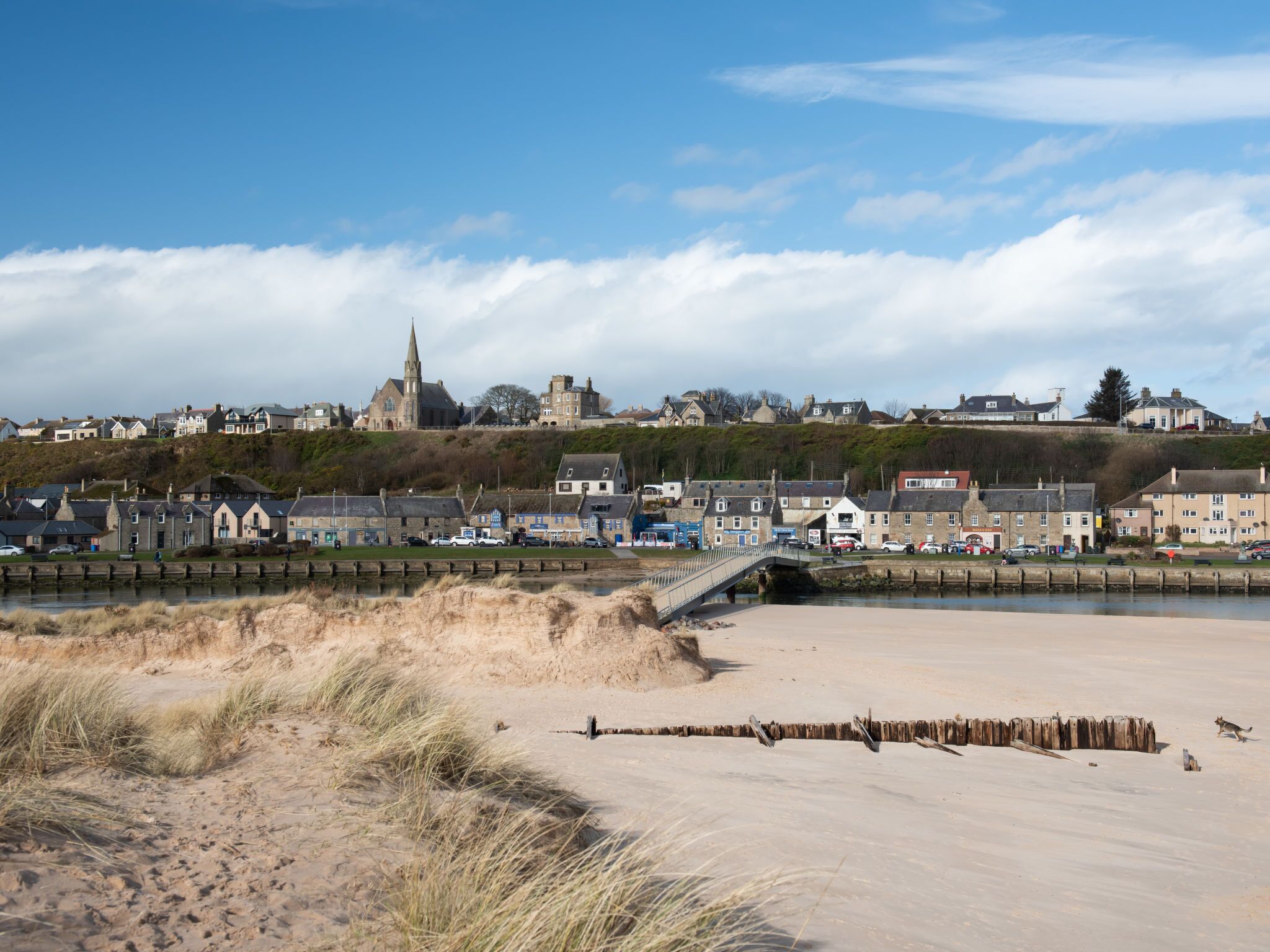 A coastal town with a prominent church, sandy beach, and a bridge connecting the shore to the town.