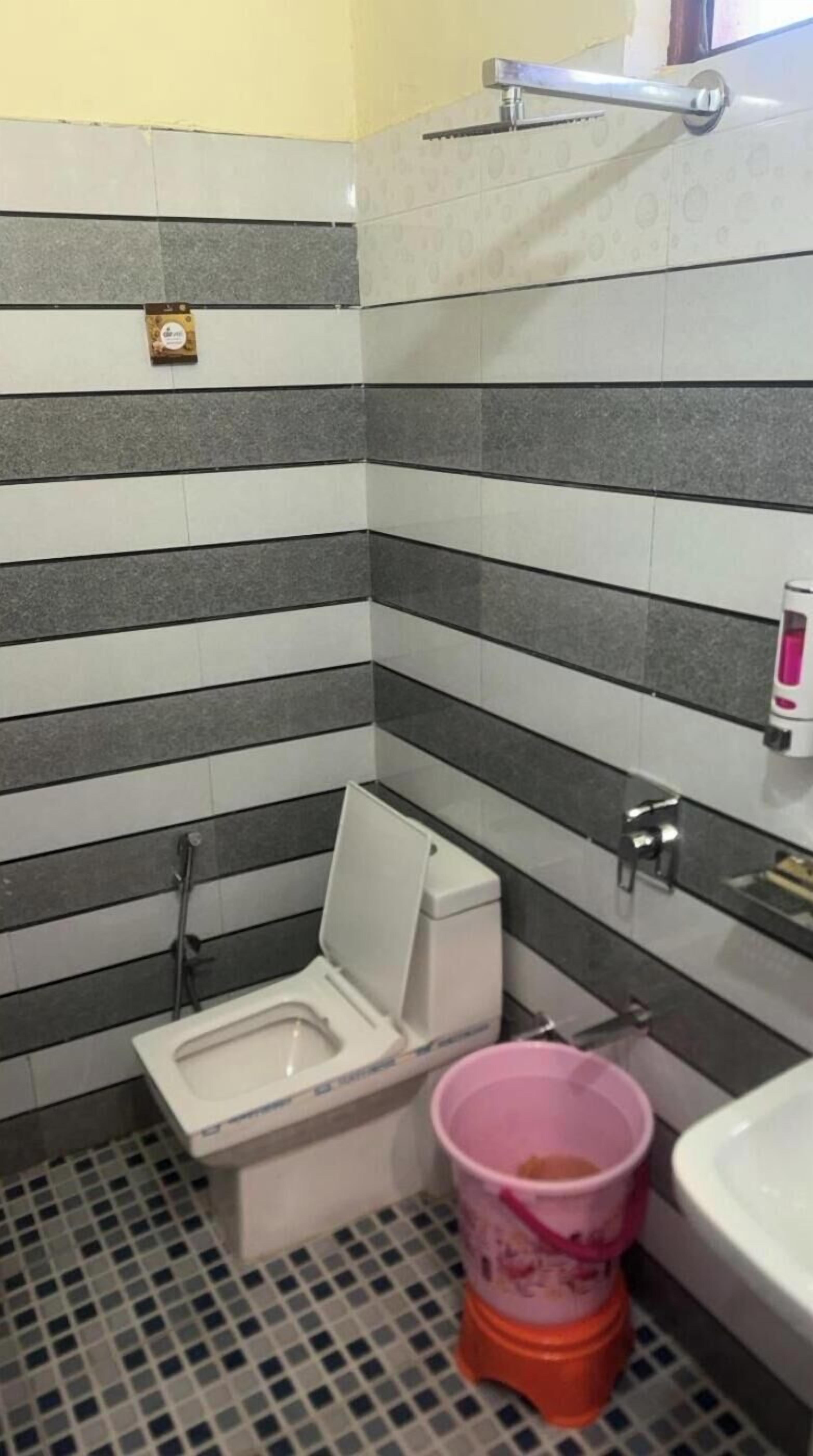 A small bathroom with a toilet, a sink, and a pink bucket.