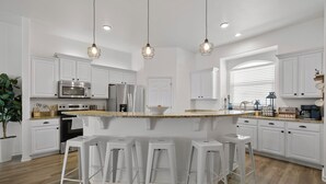 Een moderne keuken met witte kasten, een centraal eiland met barstoelen, roestvrijstalen apparatuur en hanglampen.