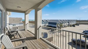 Een balkon met stoelen, met uitzicht op een parkeerplaats en strandhuisjes.