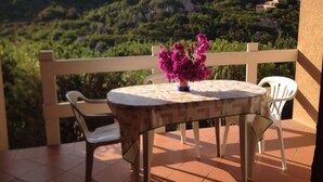 Een balkon met een tafel en stoelen, een vaas met bloemen en uitzicht op een bergachtig landschap.