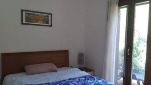 Een slaapkamer met een bed, nachtkastje, een ingelijste foto aan de muur en een raam met gordijnen.