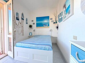 Ein Schlafzimmer mit einem Bett, einem Fenster und einem Gemälde mit einer Strandansicht.