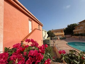 Blick auf einen Pool mit einem Gebäude mit roter Fassade und wolkenlosem, blauem Himmel.