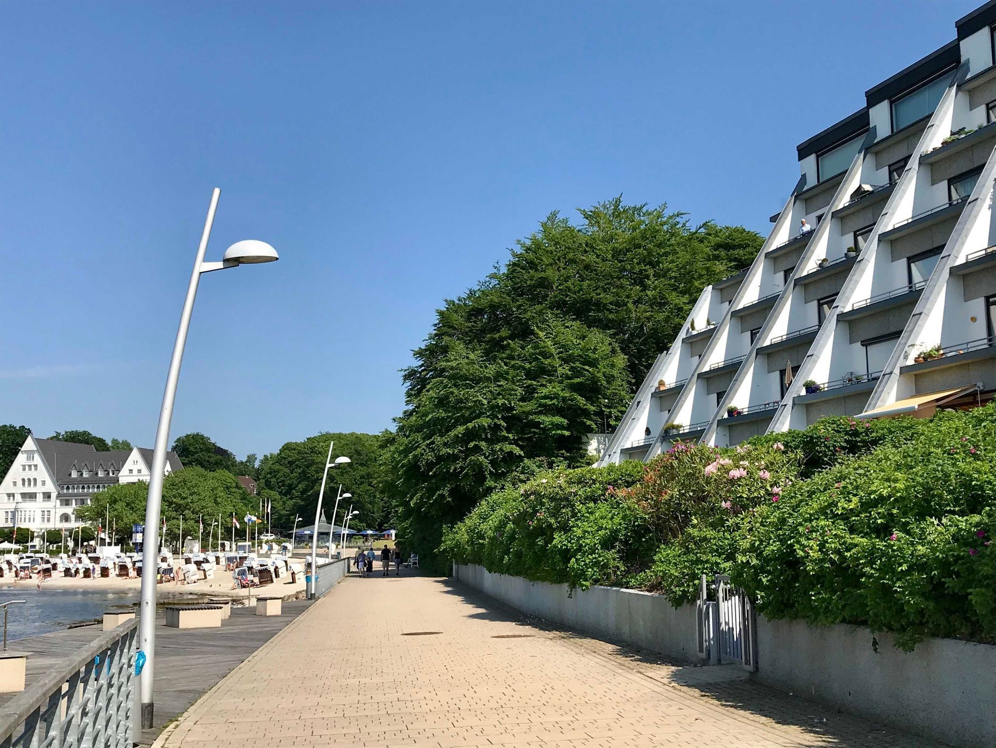 Una passejada marítima amb un edifici d'apartaments modern, un camí de fusta i una marina amb vaixells.