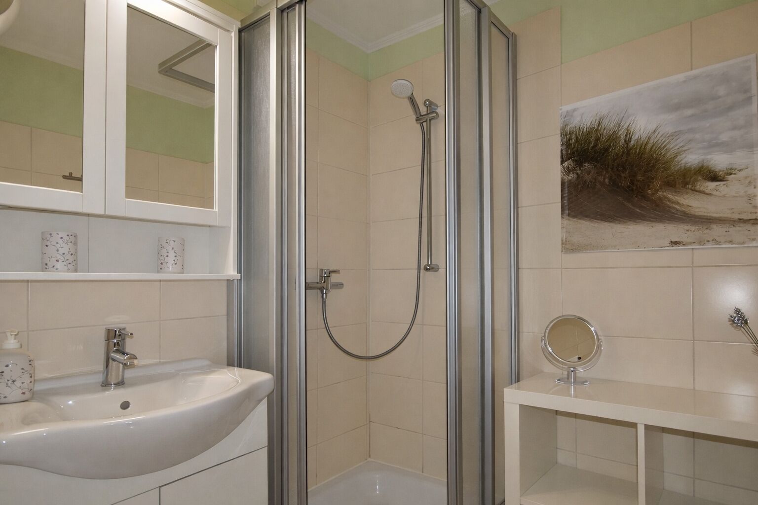 A bathroom with a shower, sink, mirror, and a painting on the wall.