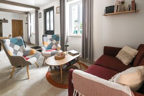 A modern living room with a red sofa, two patterned armchairs, a small coffee table, and a bookshelf with books. - "LES FOUGÈRES" Vacation Home near Baie de Somme, ideal for families (Ochancourt)