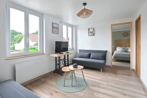A modern living room with a sofa, a television on a wooden table, and a large window. - Vacation home "LES FOUGÈRES" near Baie de Somme ideal for families (Ochancourt)