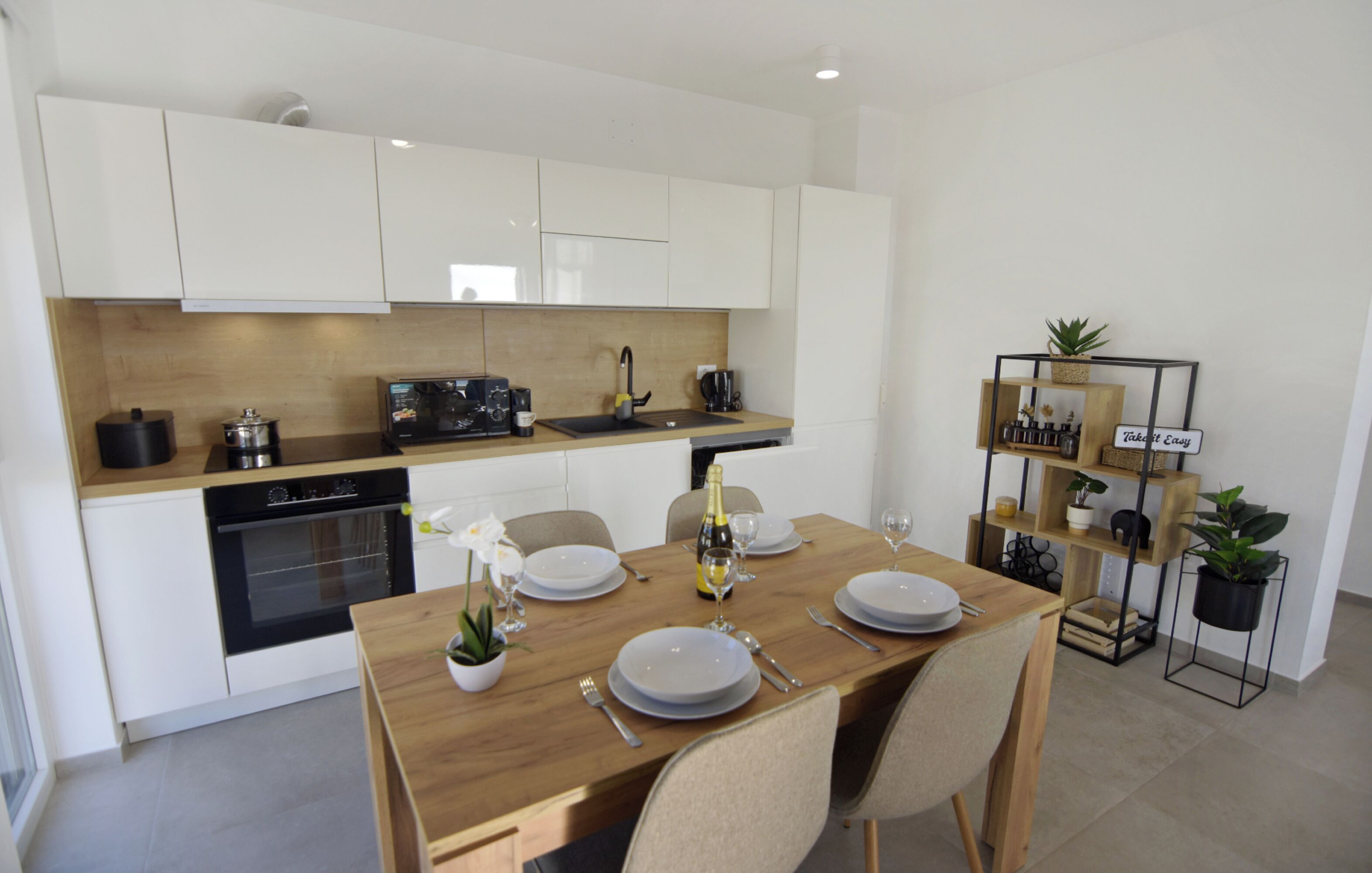 Une cuisine moderne avec des meubles blancs, un plan de travail en bois et une table à manger pour quatre personnes.