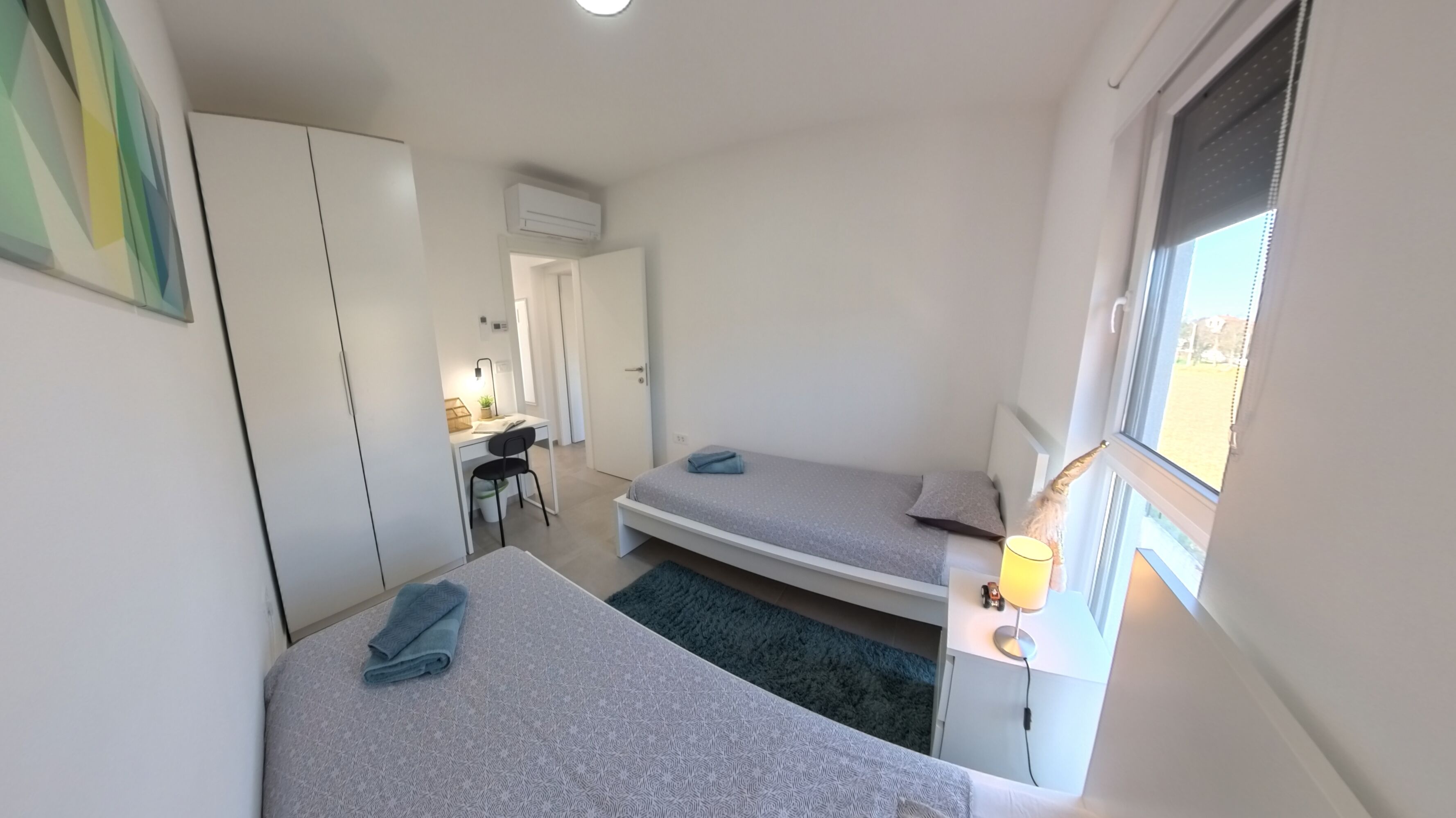 A compact bedroom with two beds, a desk, and a window.