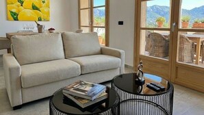 A living room with a beige sofa, a glass coffee table, and a painting of lemons. There are large windows with a mountain view. - Son Roig - Campanet more than a holiday finca (Campanet)