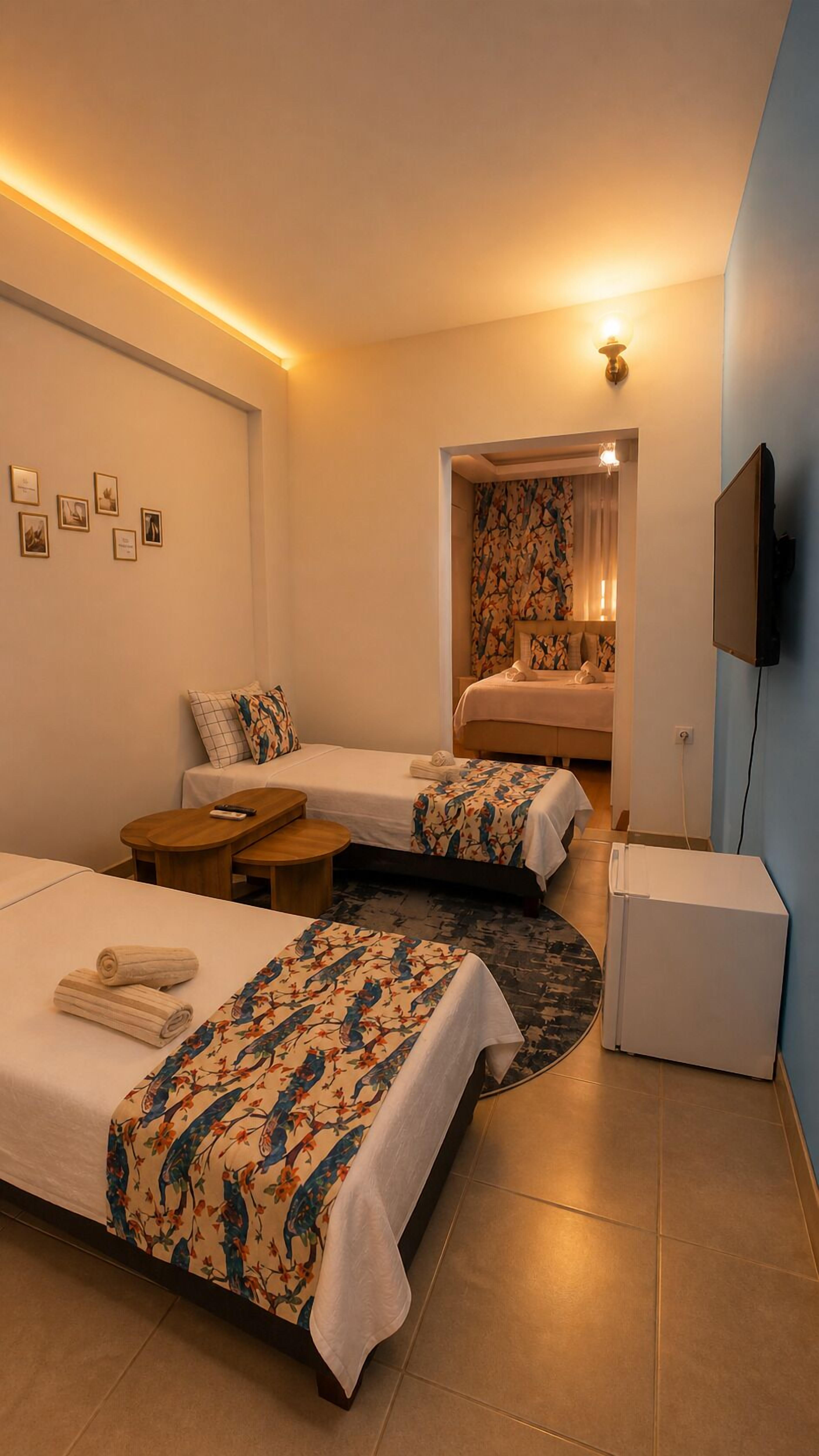 Quarto de hotel com duas camas, uma mesinha, televisão e luminária na parede.