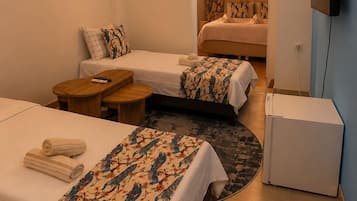 Quarto de hotel com duas camas, uma mesinha, televisão e luminária na parede.