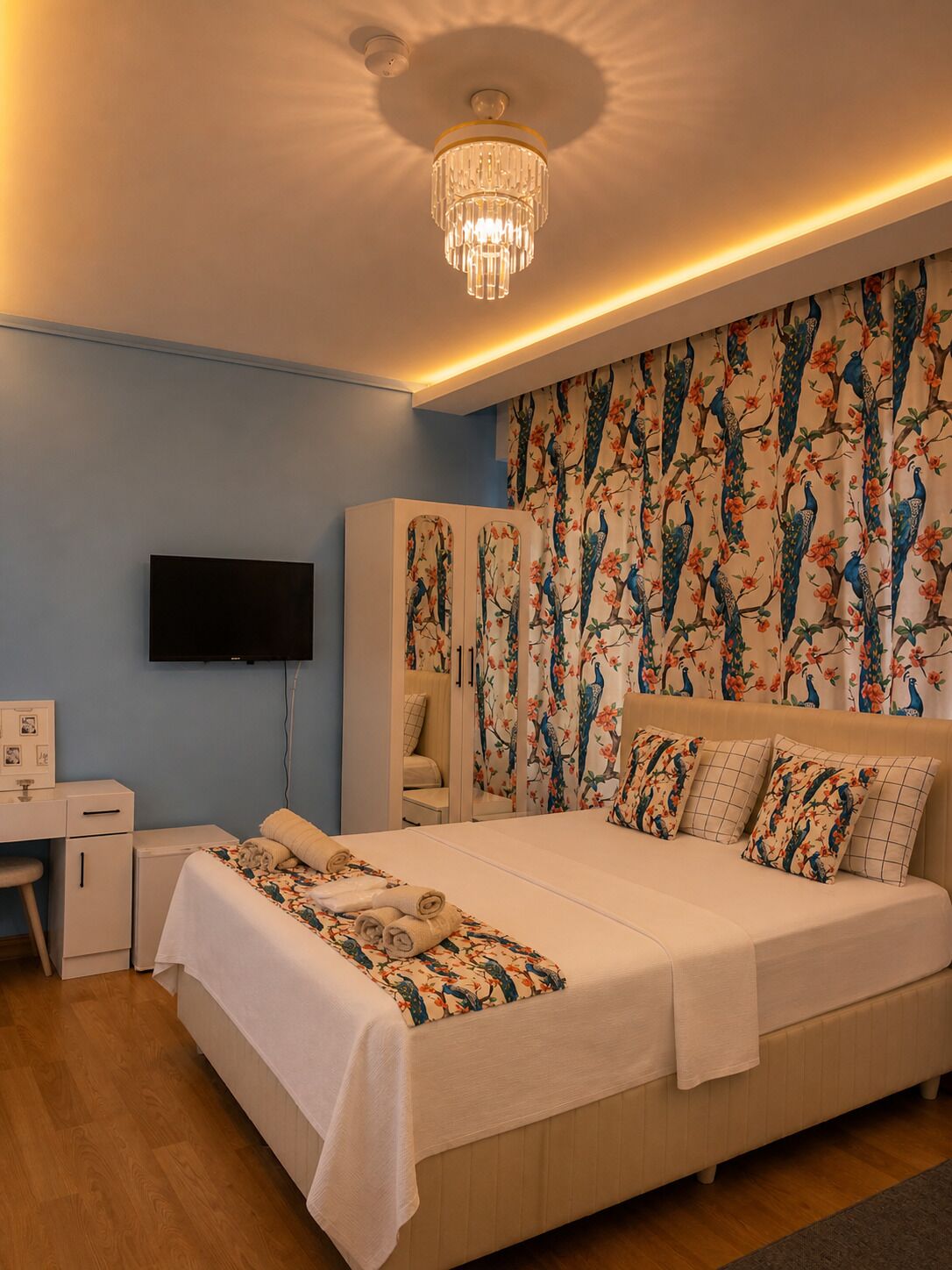 A bedroom with a large bed, a desk, a wardrobe, and a television.