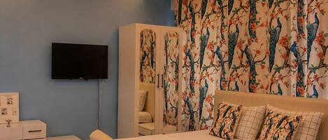 A bedroom with a large bed, a desk, a wardrobe, and a television.