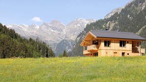 Una cabaña de madera con balcón, rodeada por un prado y montañas.