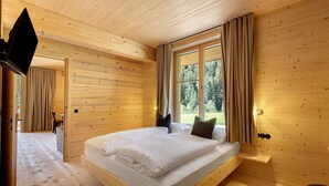 Un dormitorio con paneles de madera, una cama, un televisor y una ventana con cortinas.