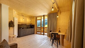 Un interior de madera con cocina, comedor y un amplio ventanal corredera que da a una terraza.