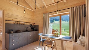 Interior de madera con cocina, mesa de comedor y vista a un paisaje verde.