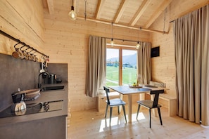 Ein Holzinterieur mit Küchenbereich, Esstisch, Stühlen und Blick ins Freie.