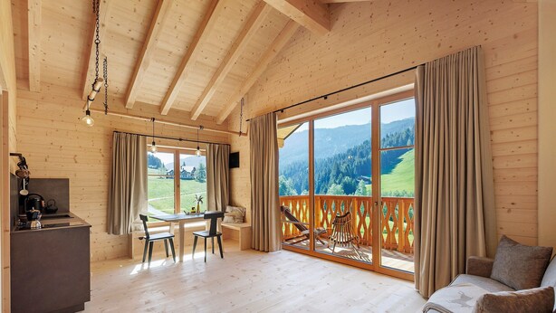 Interior de madera con comedor, sofá y balcón con vistas.