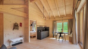 Interior de una cabaña de madera con cama, kitchenette, comedor y un banco.