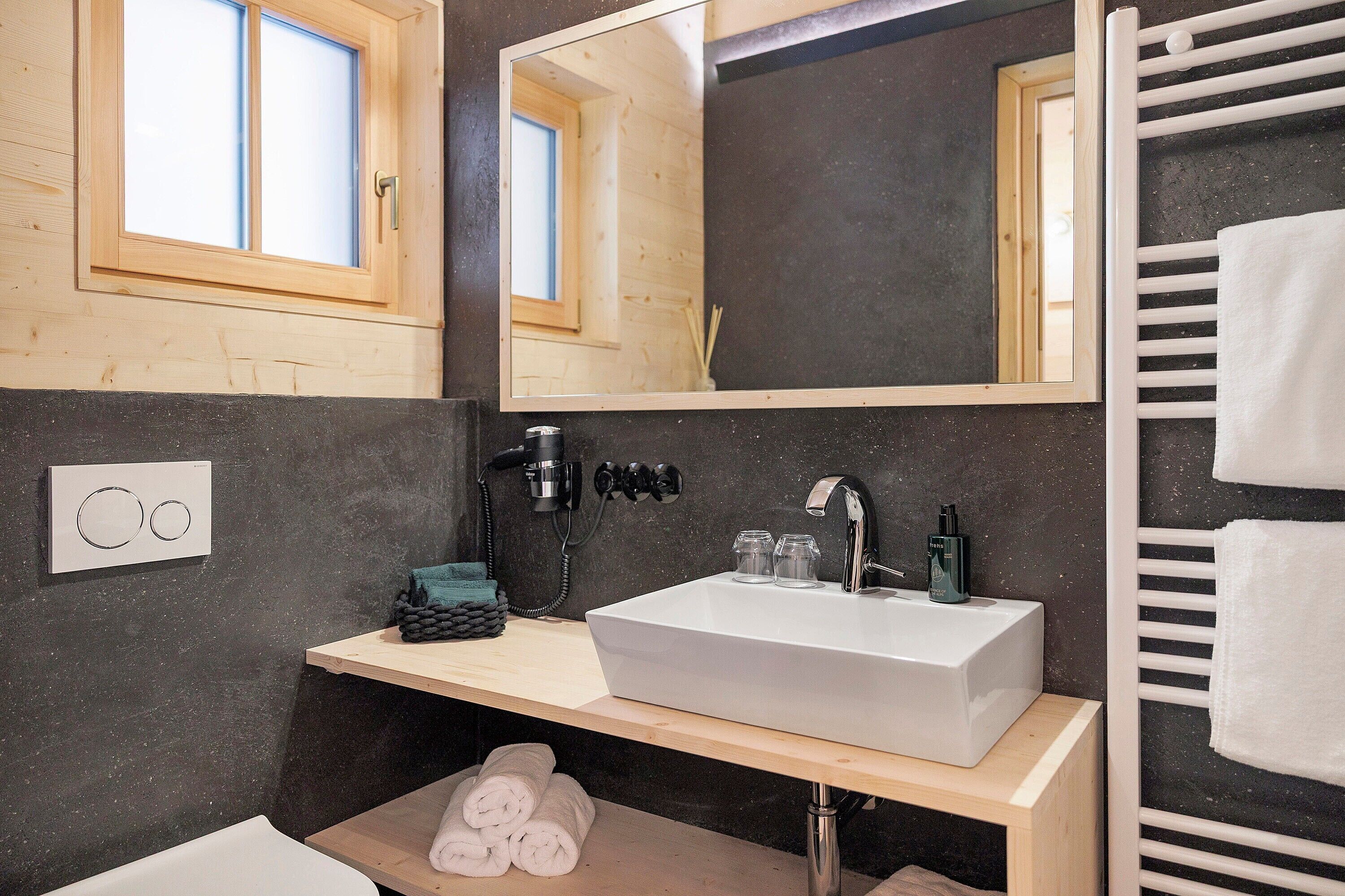 A bathroom with a wooden vanity, a large mirror, a white sink, a towel rack, and a window.