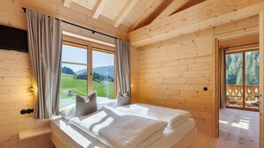 Un dormitorio de cabaña de madera con cama, cortinas y vistas al exterior.