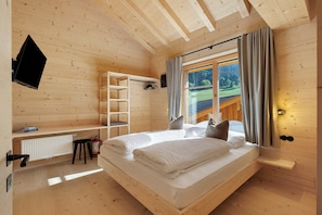 Ein Zimmer in einer Holzhütte mit Bett, Ablagefläche, Heizkörper und einem fenster mit Vorhängen.
