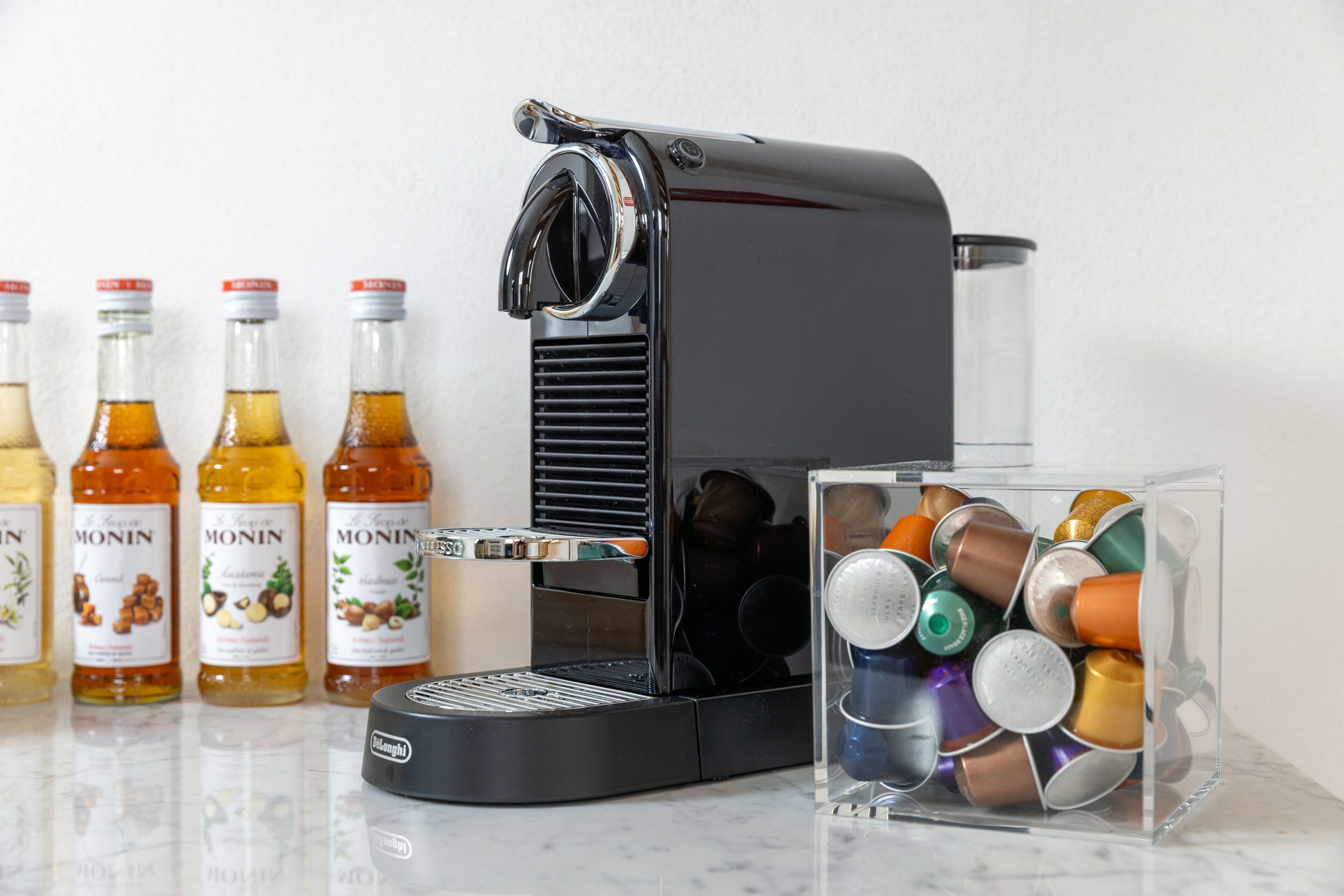 A coffee machine with a clear container of coffee capsules in front of it.