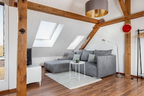 Ein Loftsesselzimmer mit grauem Sofa, einem kleinen weiĂen Beistelltisch, einer Stehlampe und einem roten dekorativen Element an der Wand.