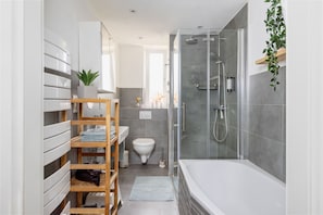 Ein modernes Badezimmer mit einer glĂ€sernen Dusche, einer weiĂen Badewanne und einem hölzernen Ablagebrett mit HandtĂŒchern.