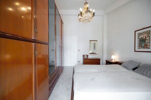 A bedroom with a wooden wardrobe, a bed with a floral bedspread, a nightstand with a lamp, and a chandelier. - Apartment Elvira sea view (Avola)