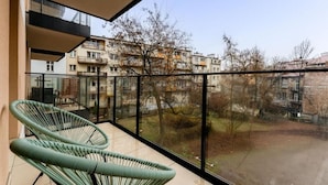 A balcony with a view of a residential area, featuring a green chair and a glass railing. - Malila Apartments Plac Bohaterów Getta (Kraków)