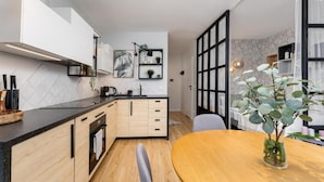 A modern kitchen with a wooden countertop, built-in oven, and a dining area with a round wooden table and a vase of greenery. - Malila Apartments Plac Bohaterów Getta (Kraków)