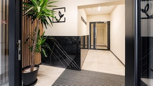 A modern interior with a potted palm tree, a black marble wall, and a tiled floor. - Malila Apartments Plac Bohaterów Getta (Kraków)