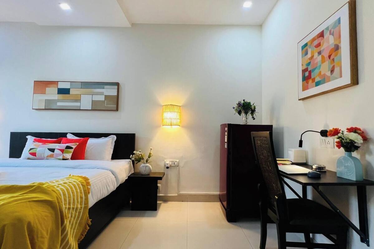 Habitación de hotel con cama, mesita de noche, lámpara, escritorio, silla y una obra de arte colgada en la pared.