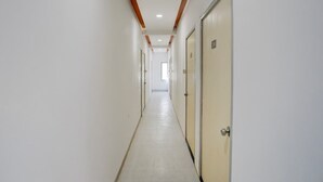 A long, narrow hallway with white walls and wooden beams on the ceiling. There are doors on the right side, one of which has a sign with the number 208. - Collection O Warje Pune Guest House (Pune)