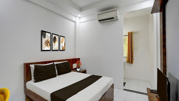 A hotel room with a wooden bed, white walls, and a ceiling-mounted air conditioner. - Collection O Warje Pune Guest House (Pune)