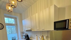 Une cuisine moderne avec des meubles blancs, des appareils en acier inoxydable et une fenêtre donnant sur les arbres.