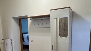 Une chambre avec un plancher en bois, des murs blancs, un lit, un radiateur et une armoire avec un miroir.