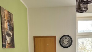 Un coin repas avec une table dressée pour quatre personnes, une porte en bois, une horloge murale et une fenêtre avec des stores.