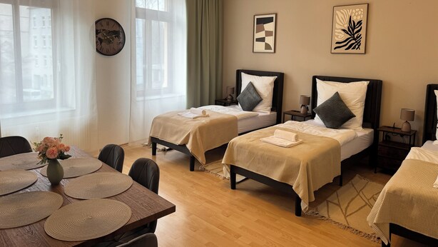 Une chambre d’hôtel avec deux lits simples, une table à manger avec des sets de table, un vase avec des fleurs et des œuvres d’art accrochées aux murs.