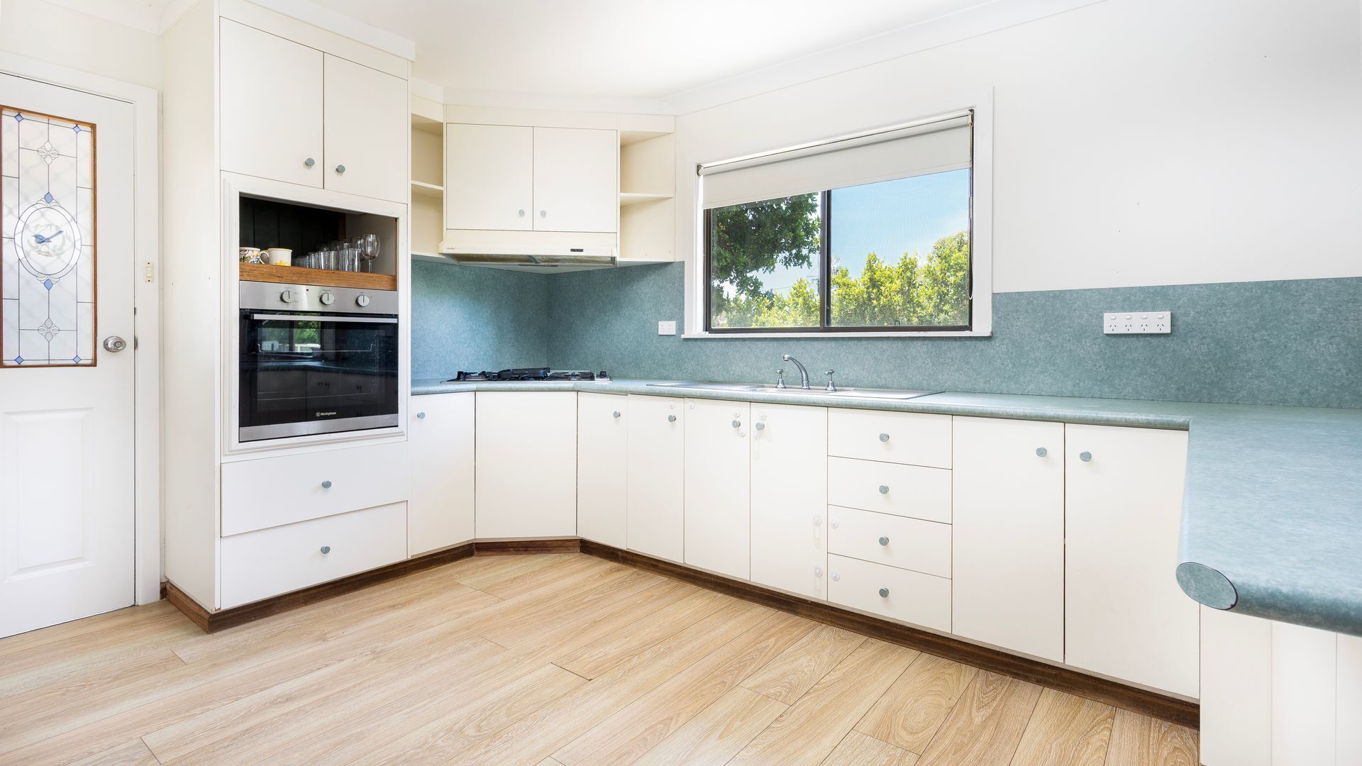 A modern kitchen with white cabinets, a built-in oven, and a window with a view of trees.