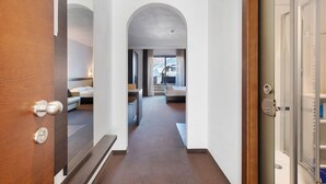 Et hotel med dør i træ, brusekabine i glas og seng med udsigt fra vinduet.