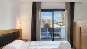 Une chambre d’hôtel avec un lit, une table de chevet, une fenêtre avec des rideaux et une vue sur des immeubles et des montagnes.