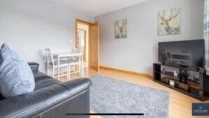 A modern living room with a grey sofa, a flat-screen TV, and a dining area with a white table and chairs. - Cosy independent studio in a small village with countryside views (Richhill)