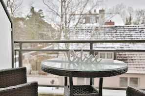 Une table ronde en verre avec un cadre en métal, une chaise en osier et une rambarde de balcon.
