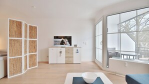 Uma sala de estar moderna com uma janela grande, uma televisão, um armário branco e um sofá azul.