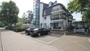 Um edifício moderno com fachada de vidro, área de estacionamento com dois carros e uma parede de pedra.